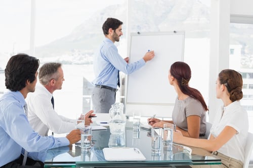 Man at a white board in a meeting with his coworkers