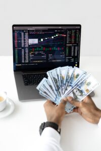 Close up of a man holding hundreds of dollars in front of a laptop