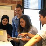 four people gathered around a laptop to collaborate at work
