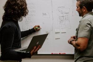 woman with laptop showing a man something on a white board