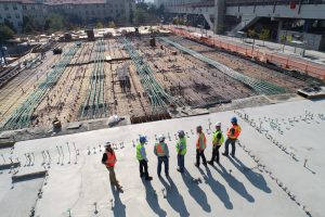 Seven construction workers looking on to a very large construction project. 