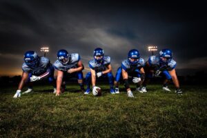 Five young men in blue American football uniforms on a grassy field