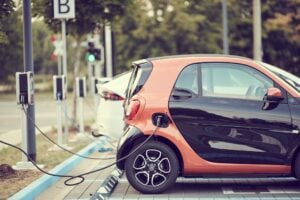 Small orange smart car charging at a charging station