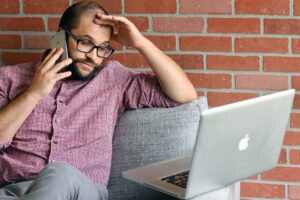 A frustrated man on the phone looking at his computer at the same time.