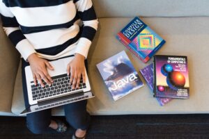 Woman working on laptop with coding books beside her