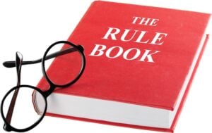 red book with the title "The Rule Book" and a pair of black reading glasses