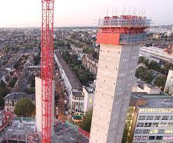 Two high-rise structures in the early phase of construction against a suburban backdrop.