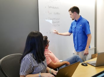 Beck Technology team members in a meeting paying attention to the presenter witting on a white board. 