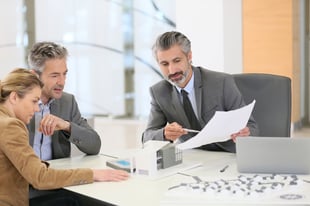 two businessmen and one businesswoman going over paperwork