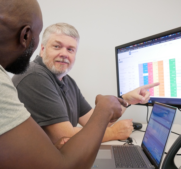 Two men review preconstruction data in front of a monitor with a spreadsheet