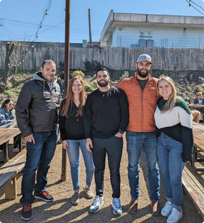 Five members of the Beck team posing for a picture in an outdoor patio with picnic tables.